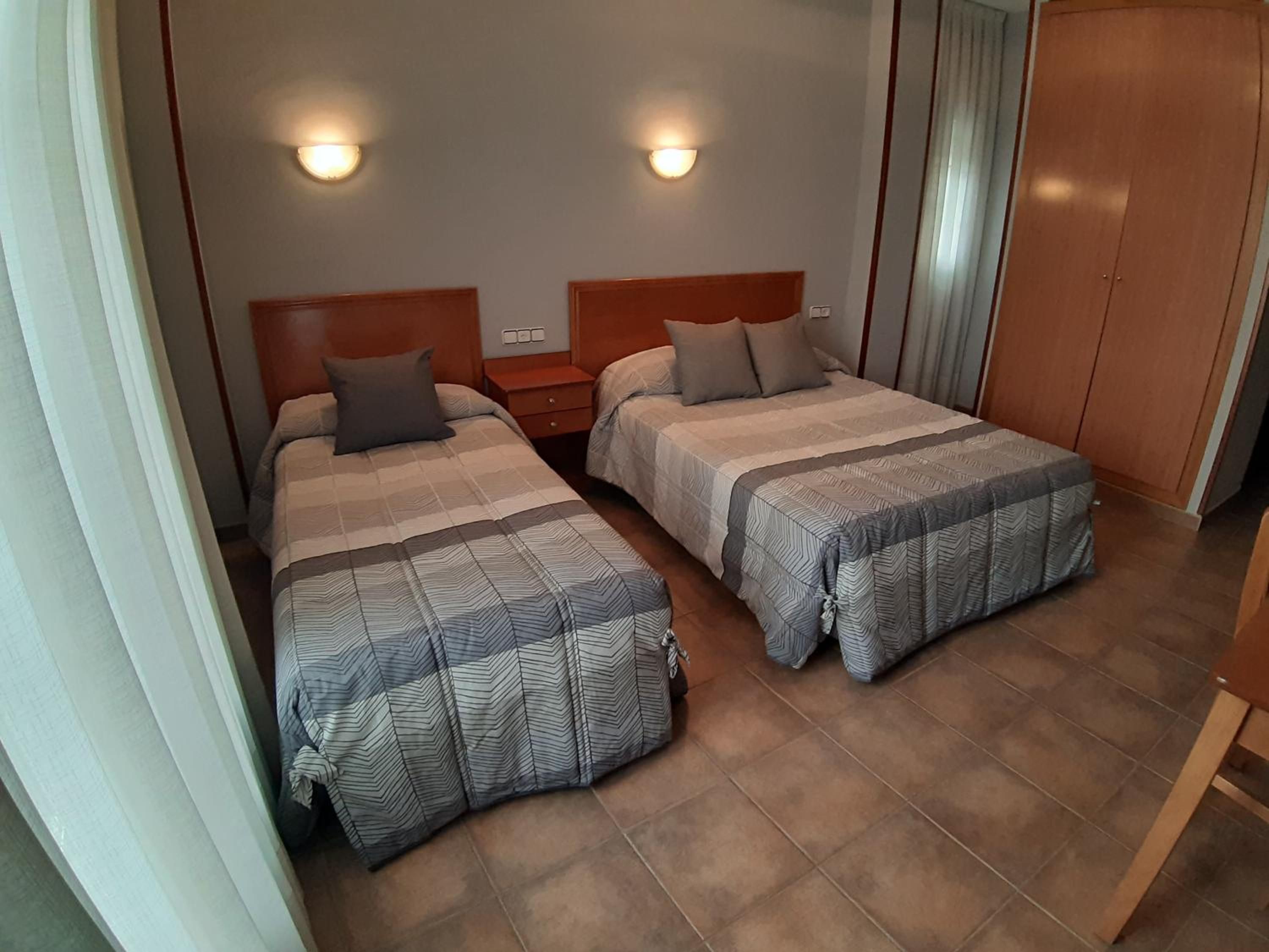 A bedroom with two beds, a nightstand, and a wardrobe.