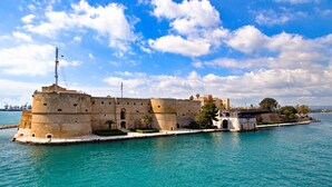 Un'antica fortificazione con un fossato, un'asta di bandiera e un ponte che conduce alla terraferma.