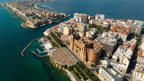 Vista aerea di una città costiera con un edificio storico importante, un porto turistico e un'ampia area aperta con un design circolare.
