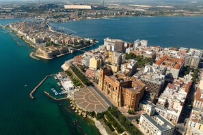 An aerial view of a coastal city with a prominent historic building, a marina, and a large open space with a circular design. - Masseria Le Mesolecchie - Ulivo Apt, Crispiano, Italy (Crispiano)