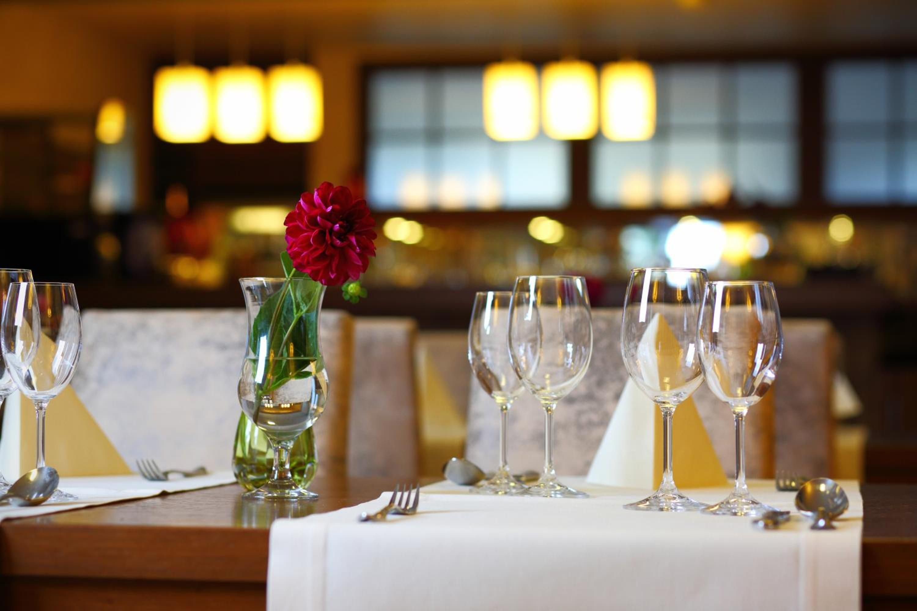 A table set with wine glasses, a vase with a red flower, and a menu.