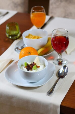 A table with a white tablecloth, a bowl of yogurt with fruits and nuts, a glass of orange juice, a glass of red wine, and a banana. - Inter Hotel (Ostroleka)