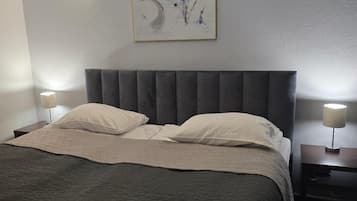 Habitación de hotel con cama, dos lámparas de noche, cabecera, un cuadro colgado en la pared y una mesita de noche.