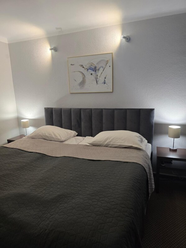 A hotel room with a bed, two bedside lamps, a headboard, a wall-mounted artwork, and a nightstand. - Inter Hotel (Ostroleka)