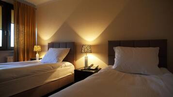A hotel room with two beds, each with a nightstand, a lamp, and a telephone.