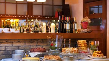 Zona de bar con una variedad de botellas, vasos y una selección de postres en una mesa buffet.