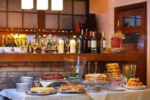 A bar area with a variety of bottles, glasses, and a selection of desserts on a buffet table. - Inter Hotel (Ostroleka)