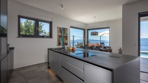 A modern kitchen with a large island, a dining area with a view, and a spacious living area with a large window. - Pool Villa Soléa /w Panoramic Sea View, Kostrena, Croatia (Kostrena)