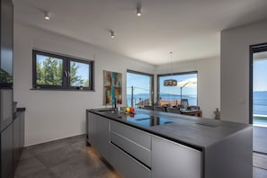 A modern kitchen with a large island, a dining area with a view, and a spacious living area with a large window. - Pool Villa Soléa /w Panoramic Sea View, Kostrena, Croatia (Kostrena)