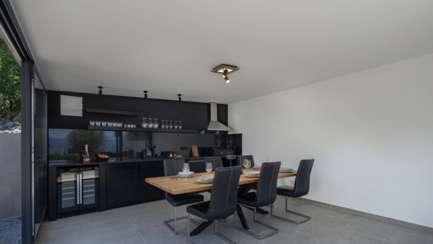 A modern kitchen with a dining area, featuring a large table, black chairs, and a built-in oven. - Pool Villa Soléa /w Panoramic Sea View, Kostrena, Croatia (Kostrena)