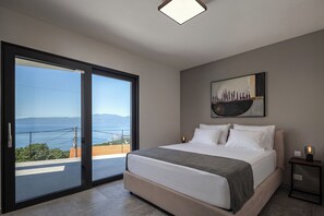 A bedroom with a bed, a painting, a nightstand, and a view through a sliding door. - Pool Villa Soléa /w Panoramic Sea View, Kostrena, Croatia (Kostrena)