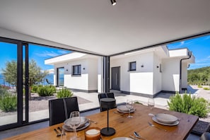 A modern dining area with a table set for two, large windows, and a view of the surrounding landscape. - Pool Villa Soléa /w Panoramic Sea View, Kostrena, Croatia (Kostrena)