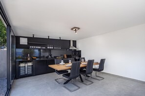 A modern kitchen with a dining area, featuring a built-in oven, black cabinetry, and a wooden dining table with four chairs. - Pool Villa Soléa /w Panoramic Sea View, Kostrena, Croatia (Kostrena)