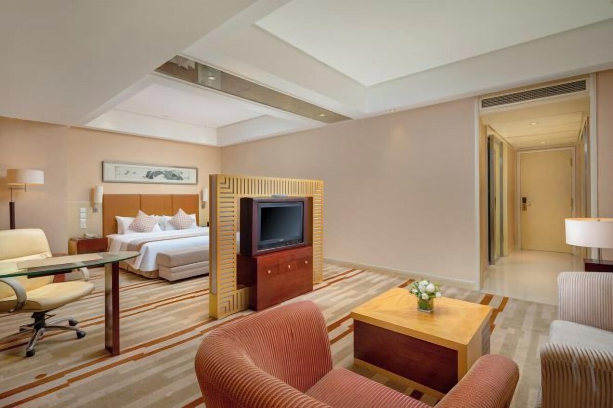 A hotel room with a bed, a TV, a desk, and a seating area.