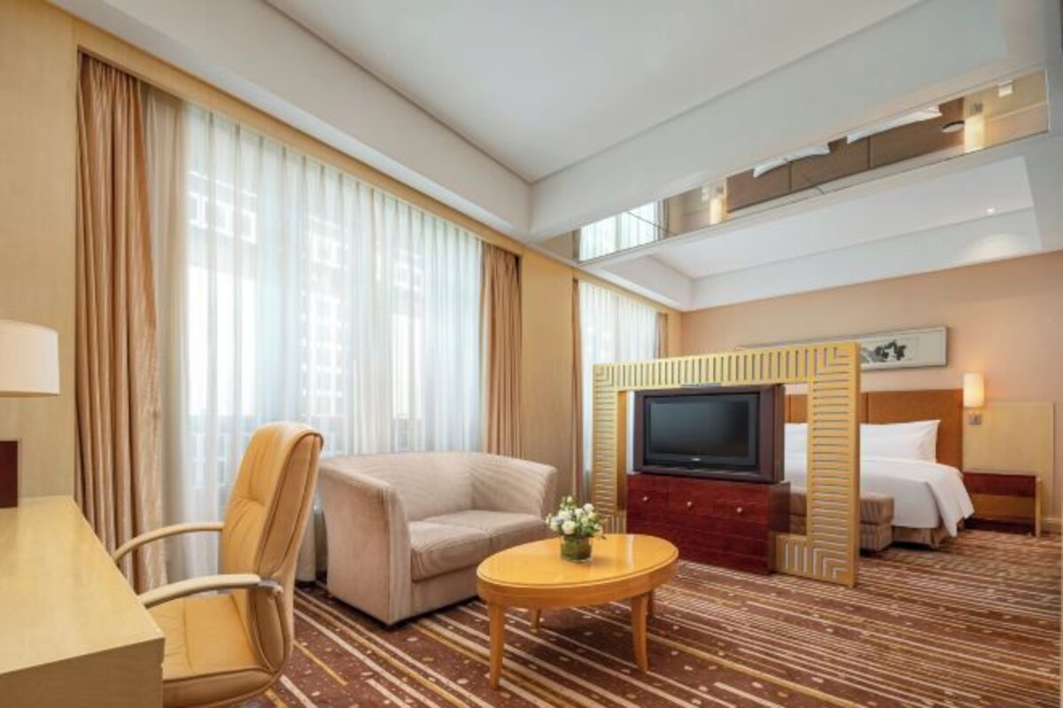 A hotel room with a sofa, armchair, TV, and a bed.