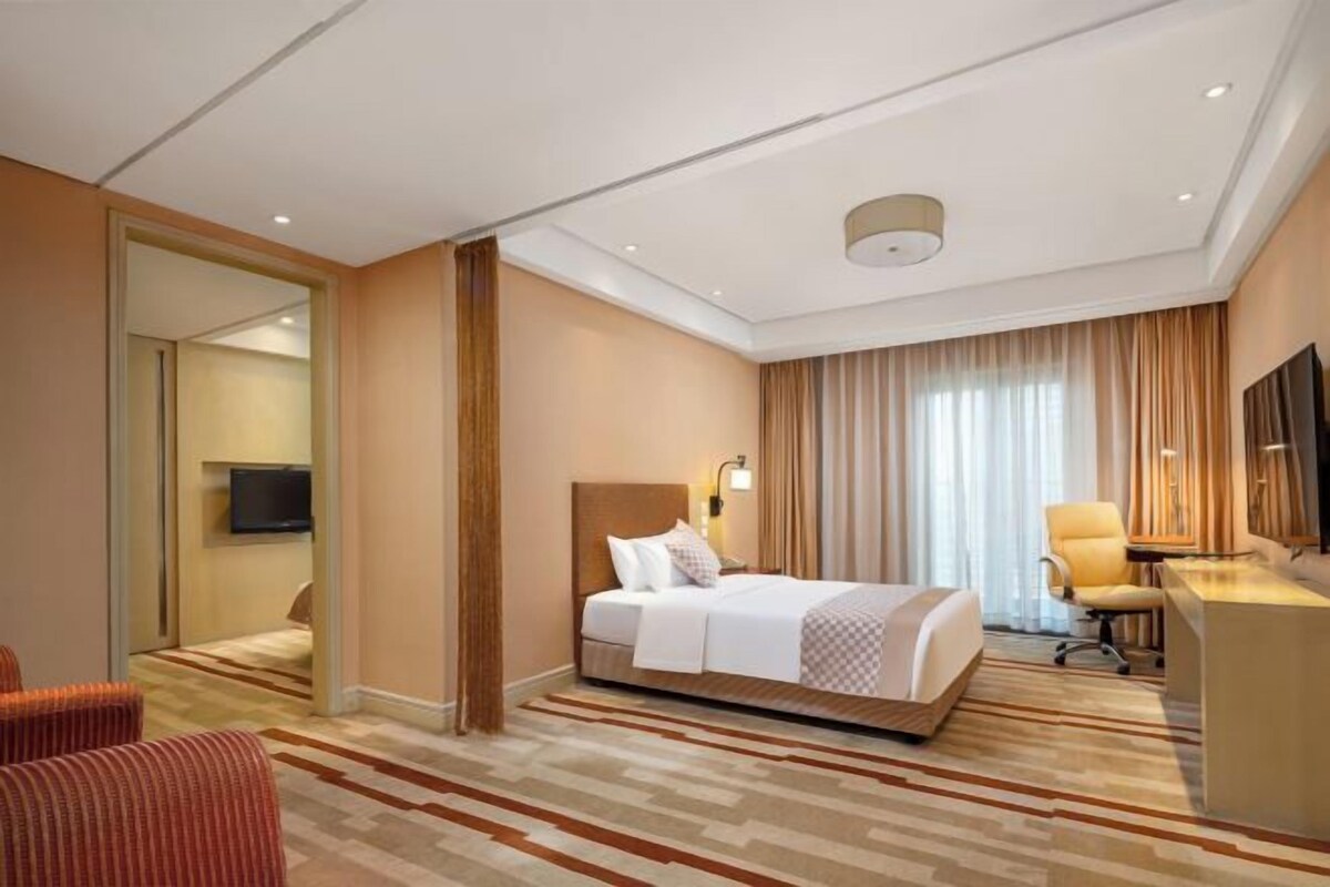 Quarto de hotel com cama, escrivaninha, televisão e cadeira.