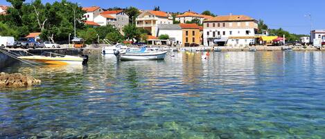 A clear waterfront with boats docked, buildings in the background, and a clear view of the water.