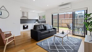 A modern apartment with a living room, kitchen, and sliding glass doors to a backyard. - Domi Rentals - The Mill Residence (Clayton South)