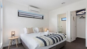 A bedroom with a bed, bedside lamps, an air conditioning unit, a mirror, and a wardrobe. - Domi Rentals - The Mill Residence (Clayton South)