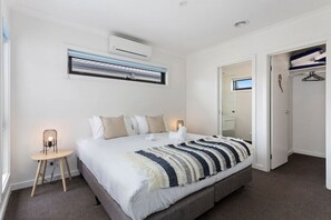 A bedroom with a bed, bedside lamps, an air conditioning unit, a mirror, and a wardrobe. - Domi Rentals - The Mill Residence (Clayton South)