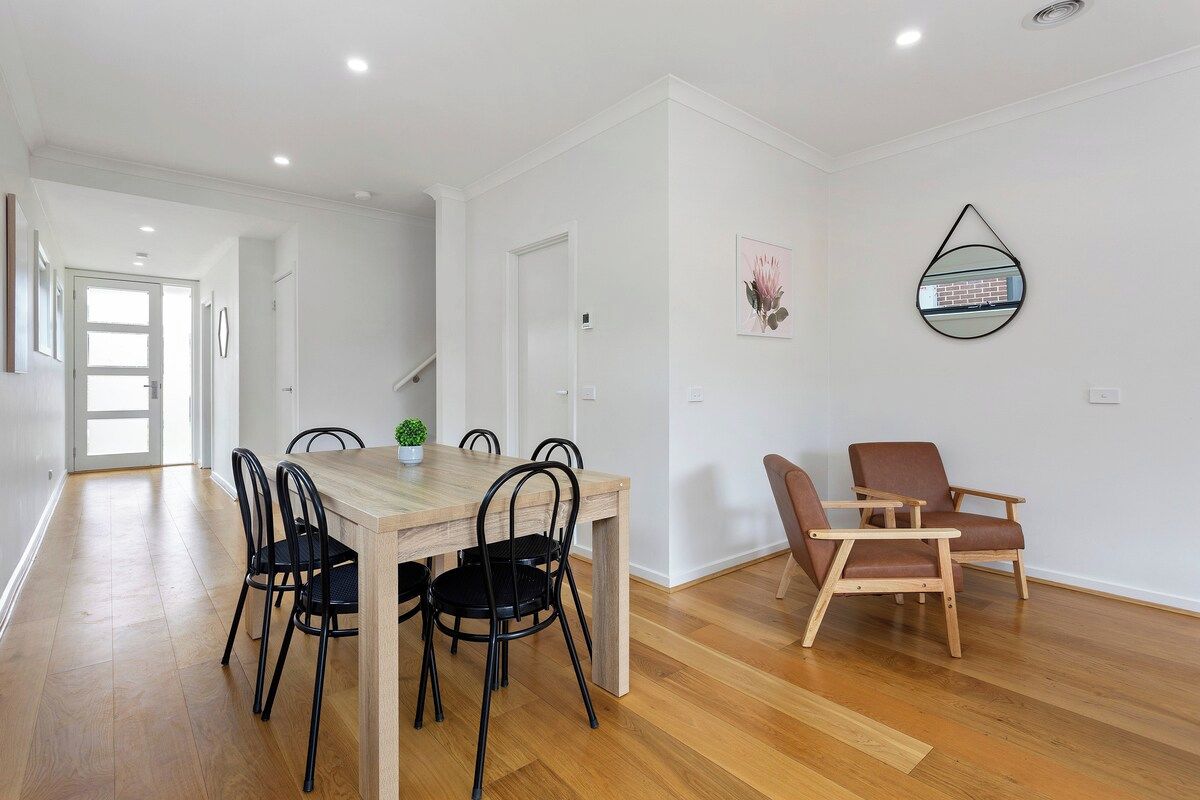A modern interior with a wooden dining table, black chairs, a brown leather chair, and a wall-mounted mirror.
