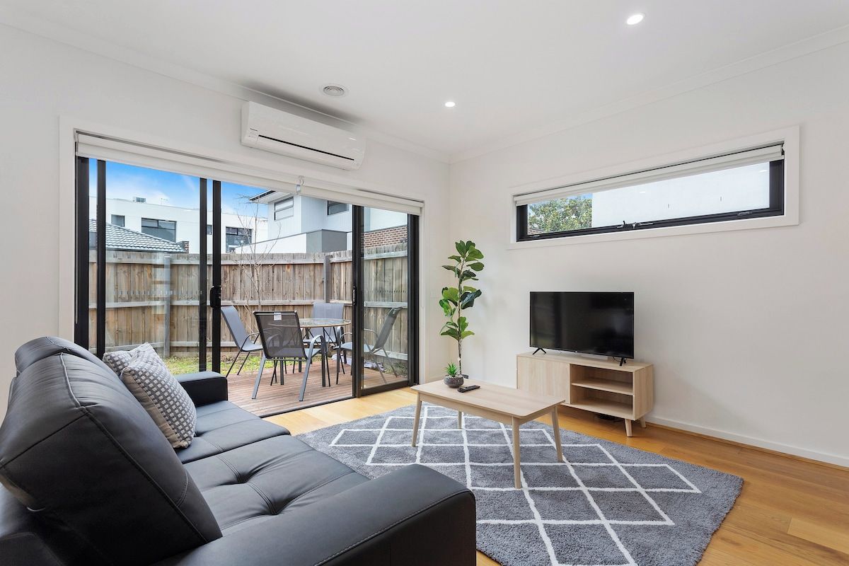 A modern living room with a sofa, TV, and a view of the backyard.