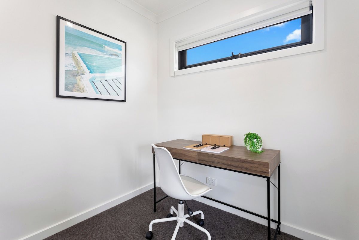 A room with a desk, chair, framed picture, and a window with a view.