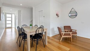 A dining area with a wooden table and chairs, a potted plant, and a brown leather chair. - Domi Rentals - The Mill Residence (Clayton South)