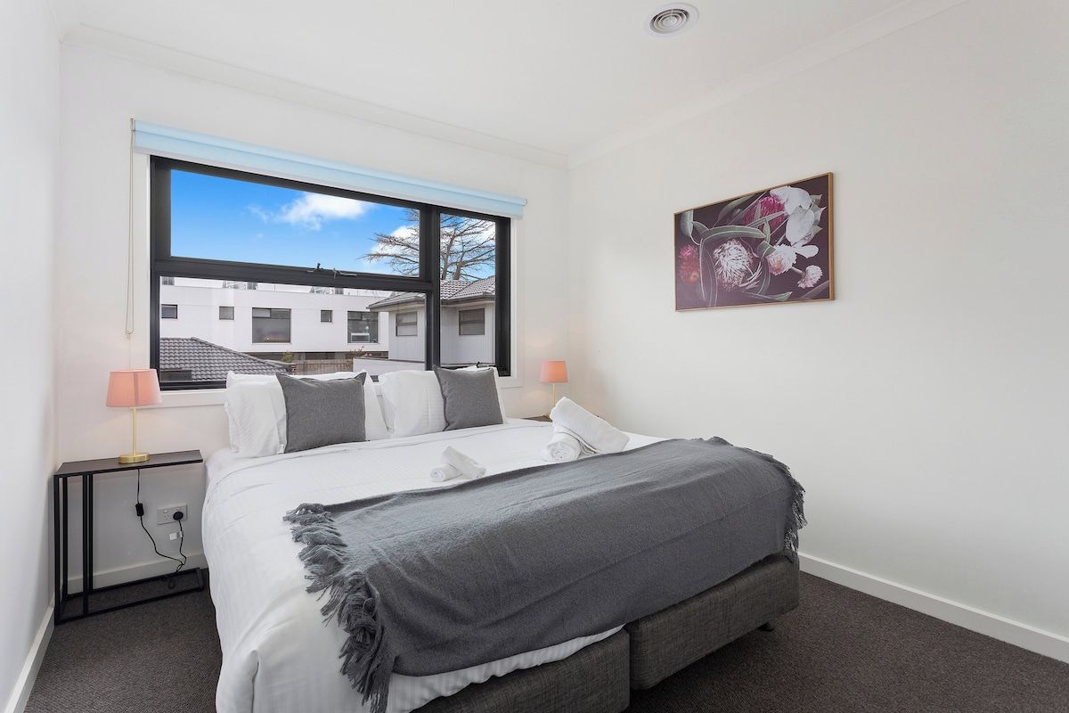 A bedroom with a bed, bedside lamps, a window, and a wall-mounted artwork.