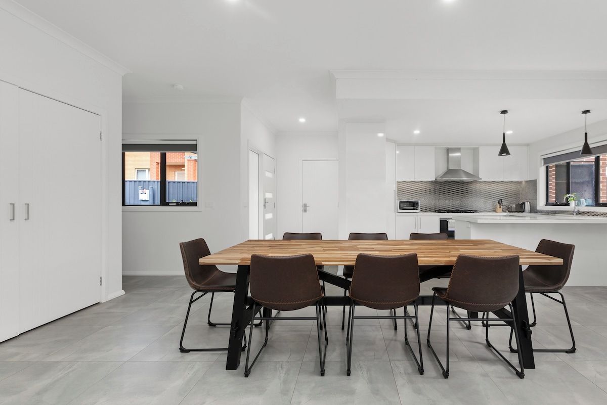 A modern kitchen with a large island, white cabinetry, and a dining area with a wooden table and chairs.