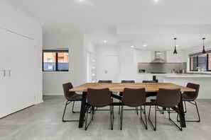 Une cuisine moderne dotée d’un grand îlot central, de meubles blancs et d’un coin repas avec une table et des chaises en bois.