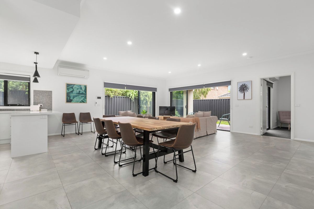 A spacious living area with a dining table and chairs, a kitchen area with a white countertop, and a large window providing a view of the outdoors.