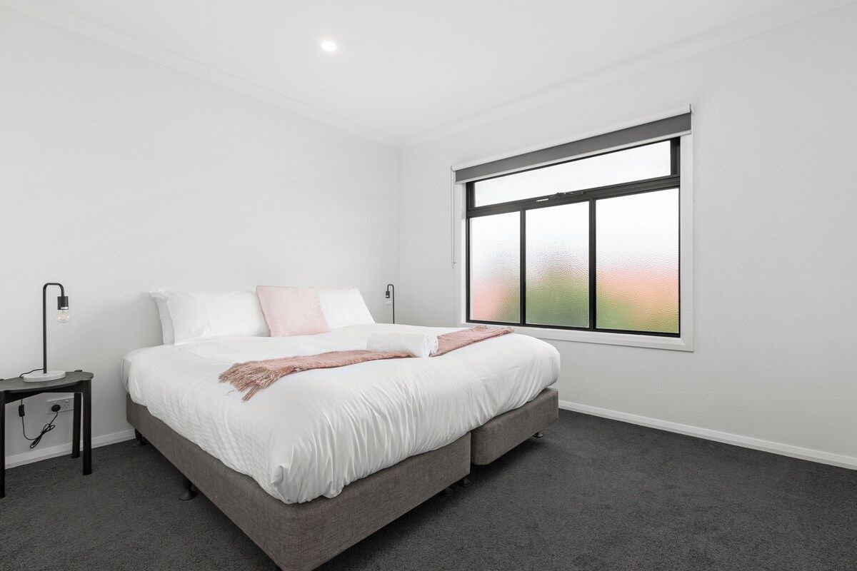 A bedroom with a bed, a nightstand, a window, and a carpeted floor.