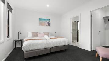 A bedroom with a bed, bedside tables, a bench, a painting, and a glass door leading to a bathroom.