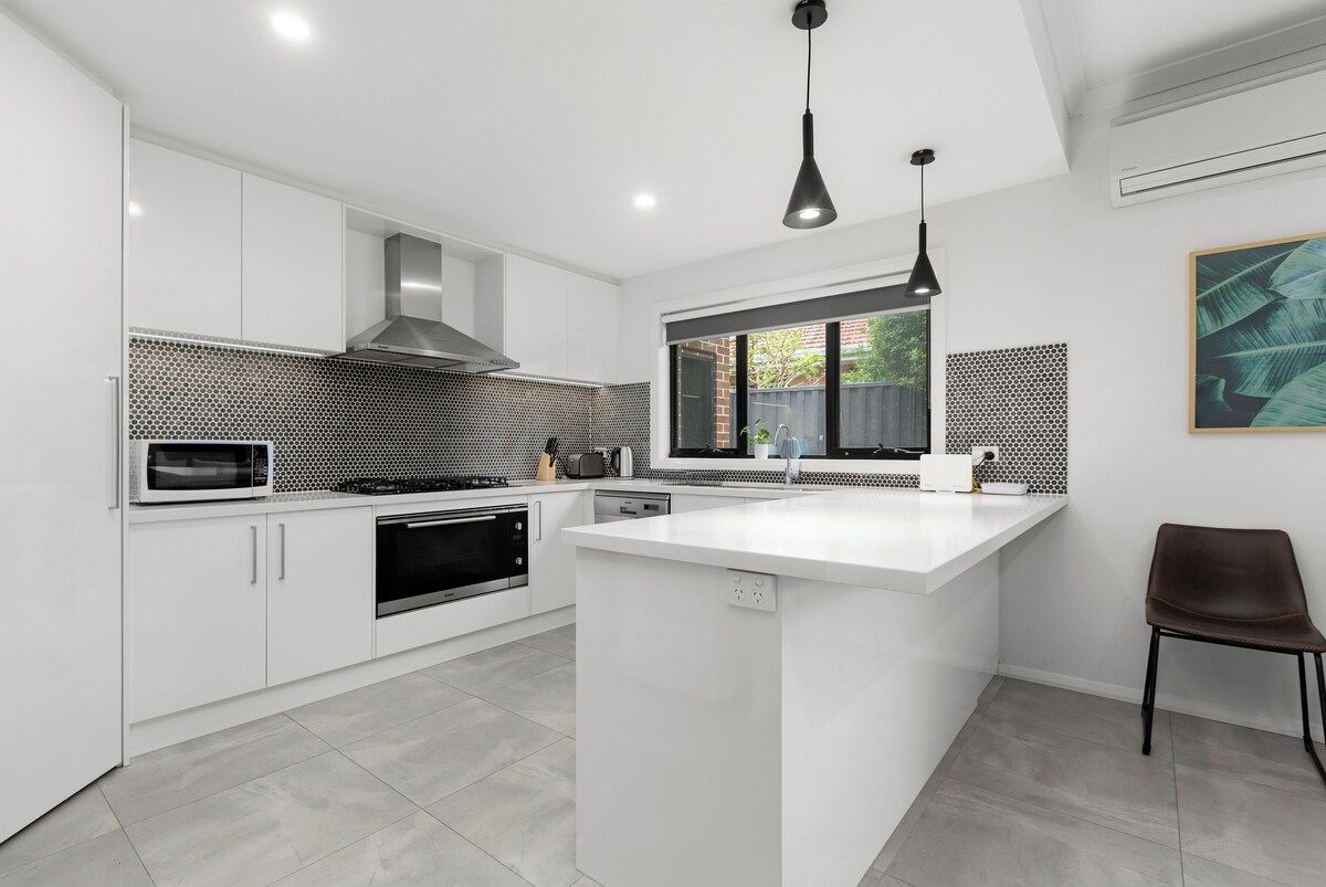 A modern kitchen with white cabinetry, a central island, a microwave, and a stove.