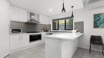 A modern kitchen with white cabinetry, a central island, a microwave, and a stove.