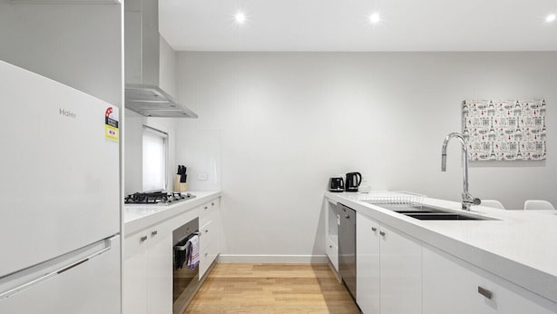 A modern kitchen with white cabinets, a stove, a sink, and a coffee maker. - Domi Rentals - The Atkinson Home (Chadstone)