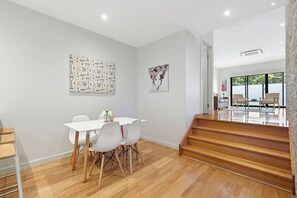 A modern interior with a dining area, wooden staircase, and artwork on the walls. - Domi Rentals - The Chadstone Homes (Chadstone)