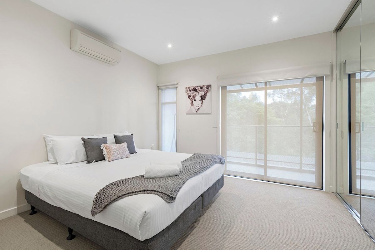 A modern bedroom with a large bed, a window, and a sliding glass door leading to a balcony.