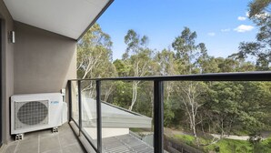 A balcony with a view of trees, a glass door, and an air conditioning unit. - Domi Rentals - The Atkinson Home (Chadstone)