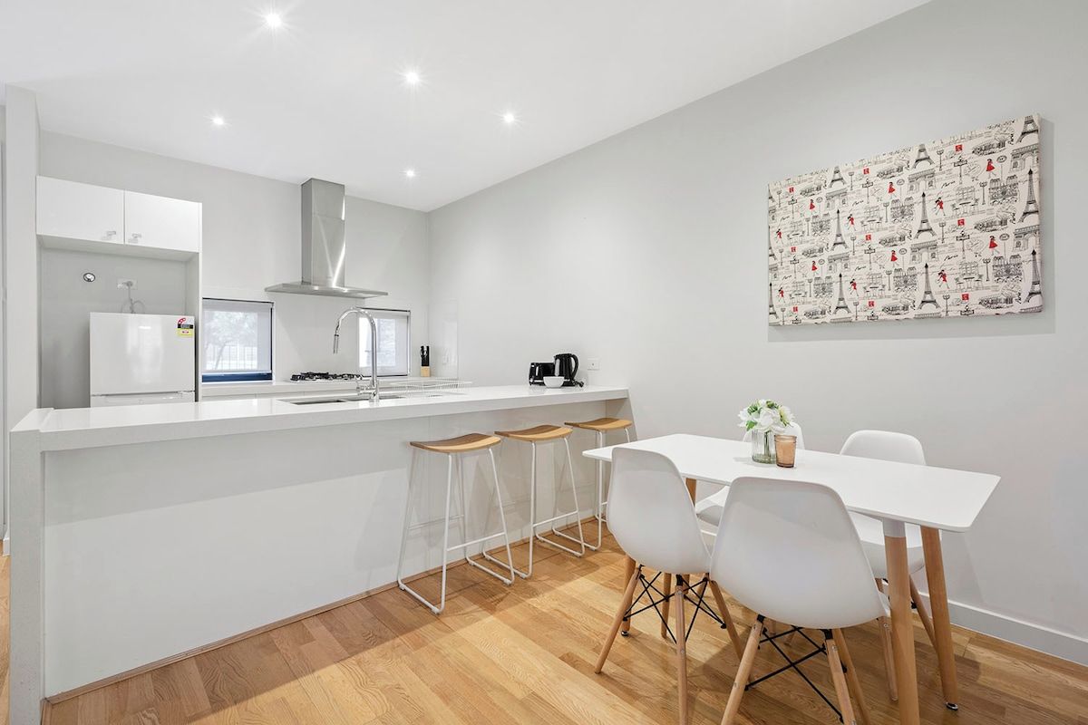 Une cuisine moderne avec un plan de travail blanc, des tabourets de bar et une table à manger avec des chaises.