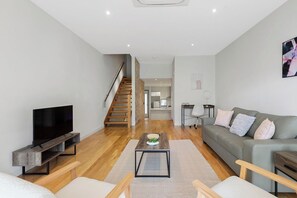 A modern living room with a flat-screen TV, a sofa, a coffee table, and a staircase leading to an upper level. - Domi Rentals - The Chadstone Homes (Chadstone)