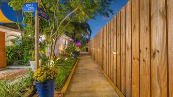 Un camino bordeado por una valla de madera y plantas en macetas, que conduce a un edificio con un letrero que indica 'King's Cove' y 'Queen's Oasis'.