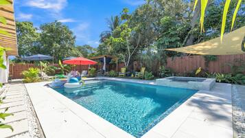 Una piscina rectangular con agua azul cristalina, rodeada por un solárium con baldosas y protegida por una pérgola.