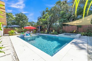 A rectangular swimming pool with clear blue water, surrounded by a tiled deck, and shaded by a canopy. - Blue Lizard Men-Only 1/1 Unit with Heated Saltwater Pool and Tropical Backyard (Oakland Park)