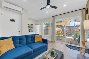 A modern living room with a blue sofa, a ceiling fan, and a view of the outdoor patio. - Men Only Heated Pool Spa - Kings Cove @Blue Lizard (Oakland Park)