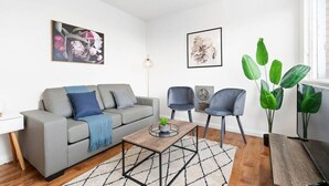 En moderne stue med en grå sofa, to lænestole, et sofabord og en stor grøn plante.