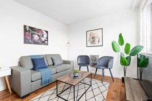 A modern living room with a grey sofa, two armchairs, a coffee table, and a large green plant. - Domi Rentals - The Balaclava Den (Saint Kilda East)