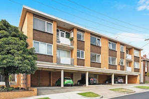 A multi-story residential building with a covered parking area and a tree in front. - Domi Rentals - The Balaclava Den (Saint Kilda East)