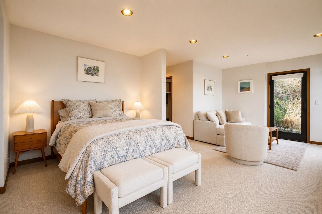 Een slaapkamer met een bed, nachtkastjes, een bankje, een sofa en een deur die leidt naar een balkon.